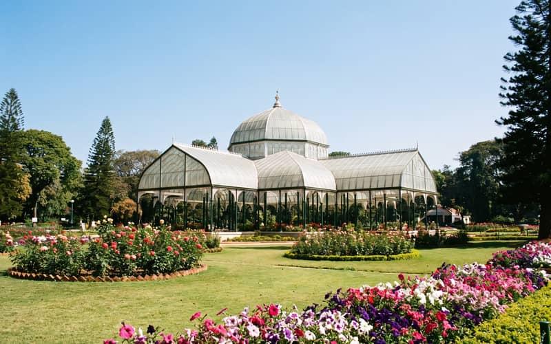 The domed Glass House at Lalbagh Botanical Garden in Bengaluru, framed by rose beds and mature trees in daylight.